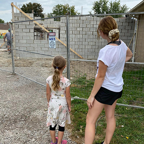 Two girls standing in front of a block wall of the school addition