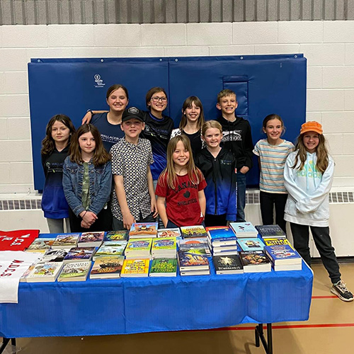 Group of kids in front of a table of books in a gym