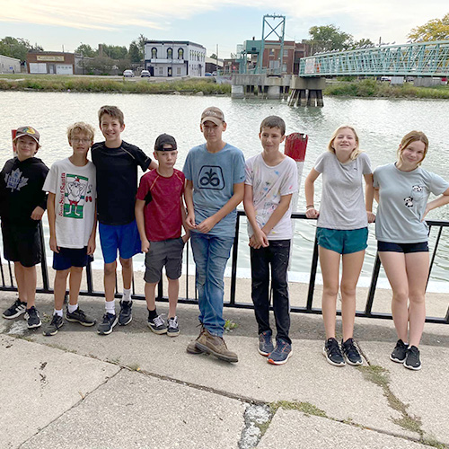 Group of kids outside in front of a river and walking bridge in Wallaceburg